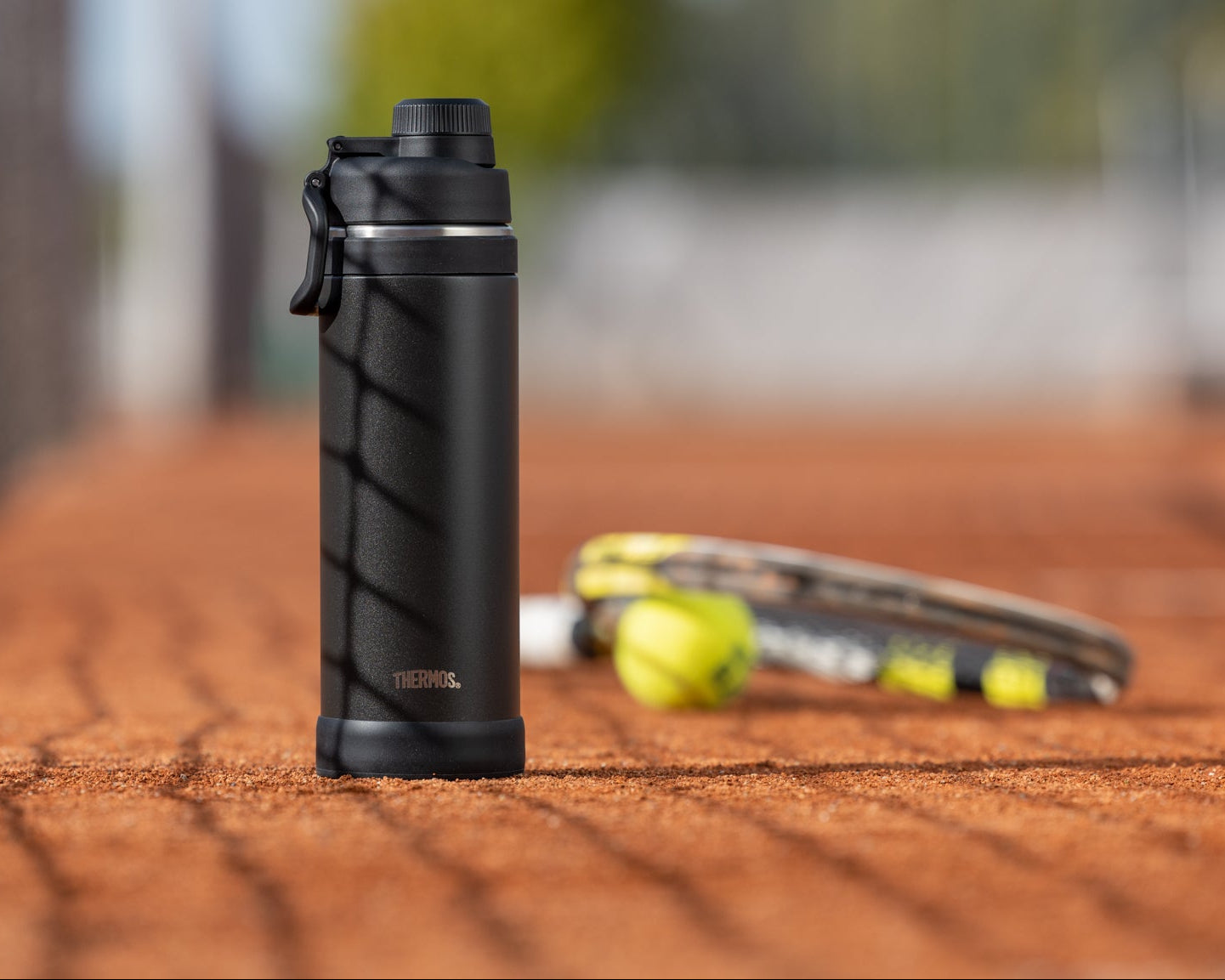 Isolierflasche auf Tennis Sandplatz mit Ball und Racket
