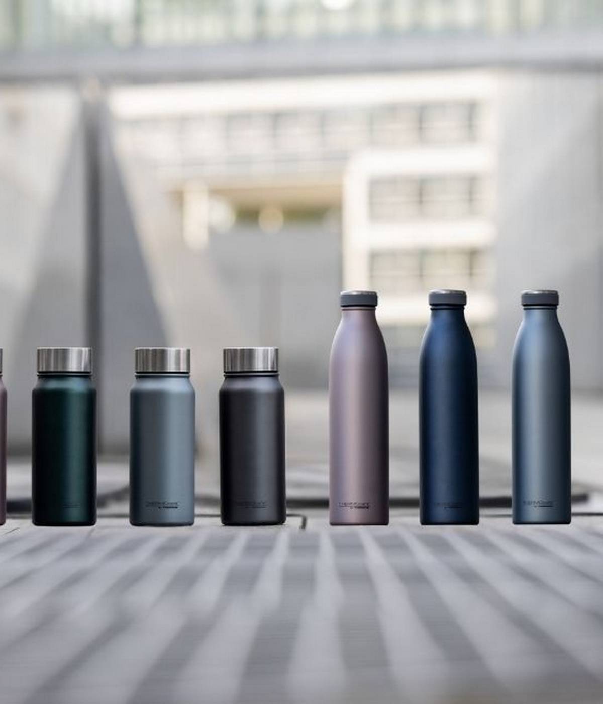 Mehrere matte THERMOcafé Flaschen in verschiedenen Farben stehen auf einer städtischen Terrasse.
